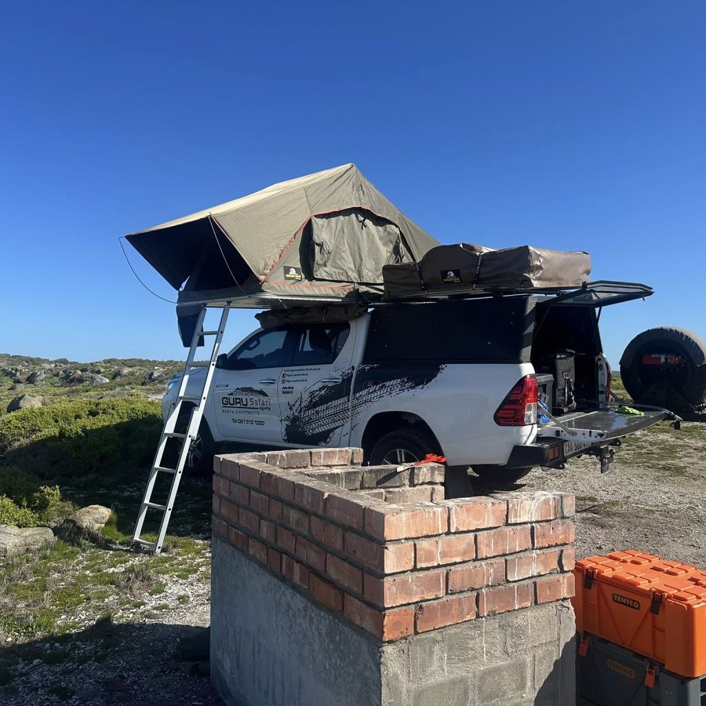 toyota hilux with dual rooftop tent setup in the coast by the fireplace